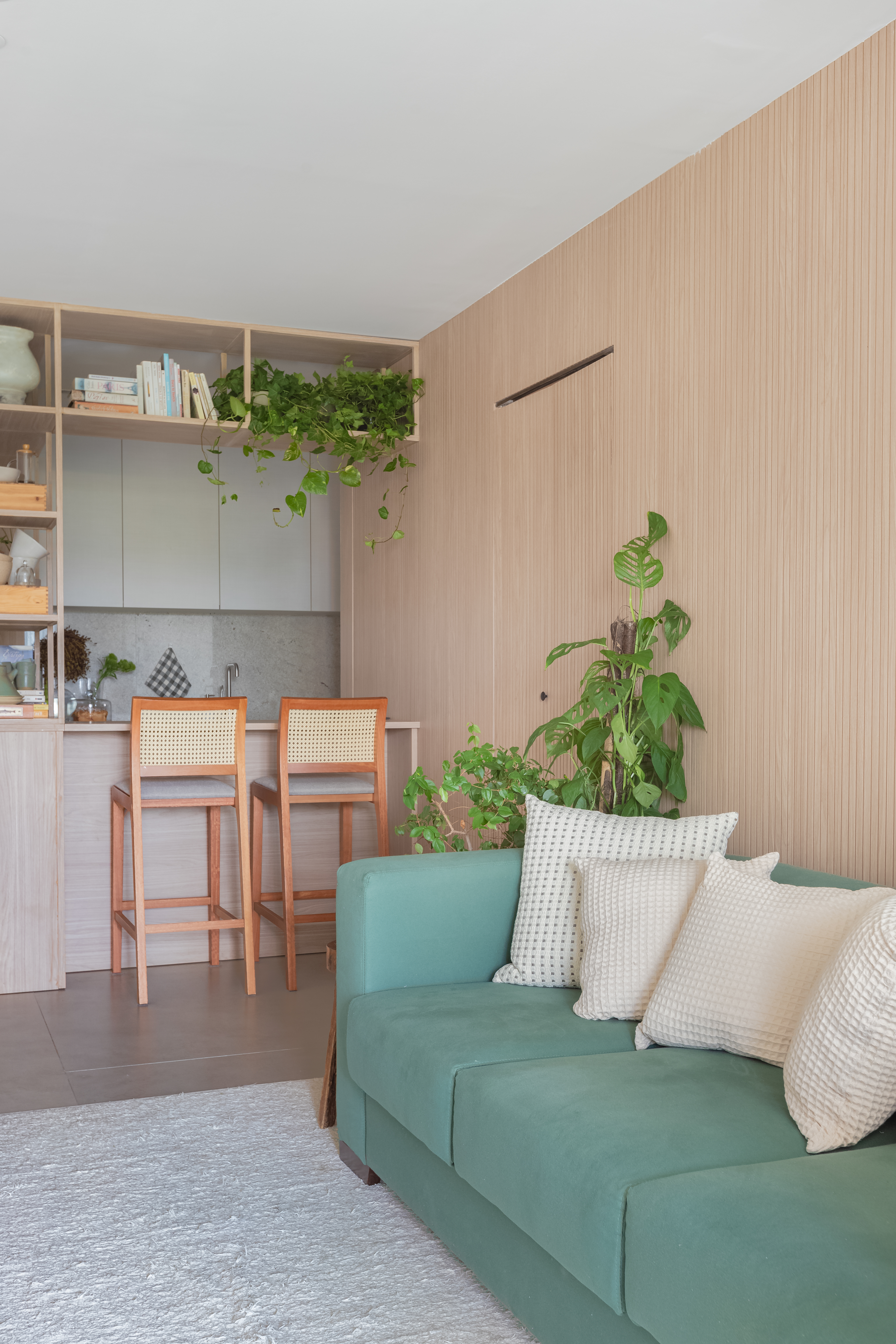 Estante emoldurando cozinha com livros e louças e sofá verde em destaque.